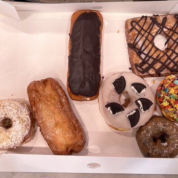 Randy’s Donuts - Lt-Rt: Butter Crumb Raised, Glazed Buttermilk, Chocolate Long John, Oreo Raised, Chocolate Crondy, Fruity Pebbles Raised & Blueberry Cake - Coffee & Tea Near Me - San Diego, California