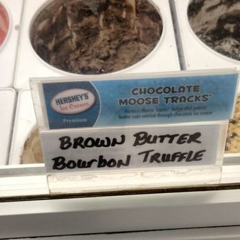 Cottage Cafe - a display of ice creams and desserts - The image shows a freezer with ice cream flavors, including Chocolate Moose Tracks. A sign in front of the freezer lists the flavors as Brown Butter Bourbon Truffle and Chocolate Moose Tracks. The background includes a gray wall, and the freezer has a white exterior with a blue and white label. - Ice Cream & Frozen Yogurt Near Me - Halethorpe, Maryland