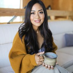 Monica Ramil, LMFT - Monica Ramil is smiling while sitting on a couch holding a coffee mug
