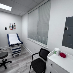 QuCiL Health™ - The image shows a compact and functional examination room at QuCiL Health™. A blue and white examination table with a gray st...