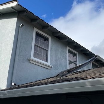 Resolution Gutter - Before Repair - A two-story house with light blue exterior walls, two windows with white trim, and a sloped roof under a partly cloudy sky. - Gutter Services Near Me - San Jose, California