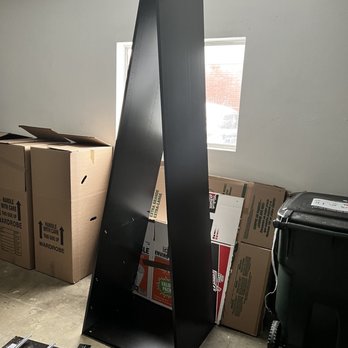 DSL Moving - A black metal shelving unit is leaning against a wall in a storage room with cardboard boxes and a trash bin nearby. - Movers Near Me