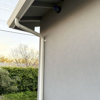 Vrumix - Ubiquiti AI Turret camera - A black security camera with a blue light is installed on the beige exterior wall of a building, near the roofline. - Home Automation Near Me - Mountain View, California