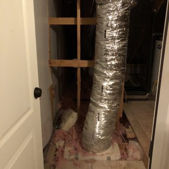 Plus58 Remodeling - Upstairs storage space entry before - An insulated metallic duct is installed in an unfinished basement or utility room, with exposed wooden framing and insulation material on the floor. - General Contractors Near Me