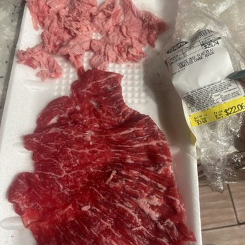 Ralphs - What a joke Ralph's has become. - The image shows raw beef and pork meat placed on a white foam tray, with the beef occupying most of the tray and the pork placed above it. The meat appears fresh and uncooked. A plastic-wrapped package with a price tag is held in the right hand, showing a total price of $25.74. The background includes a metallic surface and part of a grocery store environment. - Grocery Near Me - Temple City, California