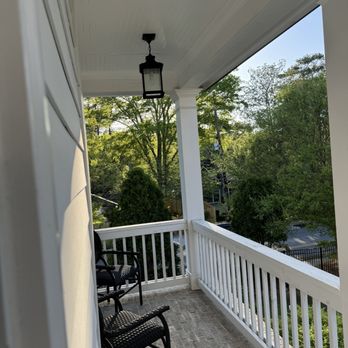 Cool Geekz - New light he installed which is obviously 2 sizes too small. - A porch with white railing and brick flooring features two black chairs and a hanging lantern, with trees and a street visible in the background. - Home Theatre Installation Near Me