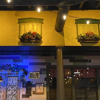 Aurelio's Pizza - Inside - The photo captures the interior of a restaurant featuring a yellow wall with decorative flower boxes and shutters. Below, there is a section with multicolored horizontal panels, illuminated by warm and blue lighting. String lights hang from the ceiling, adding to the ambiance. The scene includes a central support column and various decorative elements, creating a cozy dining atmosphere. - Pizza Near Me - Bourbonnais, Illinois