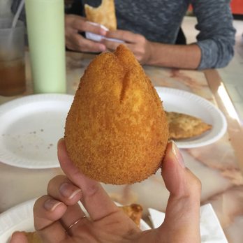 Bom DMais - a person holding a fried food item - Brazilian Near Me - Long Branch, New Jersey