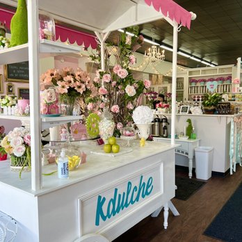 Kdulche Cafe - a white cart with flowers on it - A flower cart decorated with pink and white flowers and a pink canopy at Kdulche Cafe in Lansing, IL. - Coffee & Tea Near Me - Lansing, Illinois