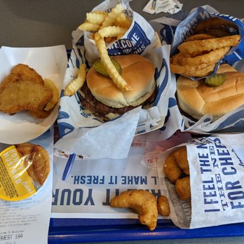 Culver's - Mushroom and Swiss Burger, fries, onion rings, and cheese curds - A fast food tray contains two burgers with pickles, a serving of crinkle-cut fries, onion rings, cheese curds, and a chicken nugget. The tray is lined with branded paper, and a receipt is visible in the corner. The food items are arranged for a meal at a casual dining or fast food restaurant. - Burgers Near Me - Gilbert, Arizona