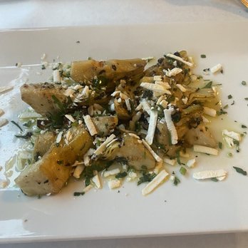 Sotto Voce - Artichoke hearts appetizer - A serving of cooked artichoke hearts is presented on a white rectangular plate, topped with shredded cheese and chopped herbs. The artichoke hearts are cut into pieces and appear to be seasoned, with some visible oil or dressing. The dish is arranged in a small pile, with a simple presentation suitable for a restaurant setting. - Italian Near Me - Brooklyn, New York