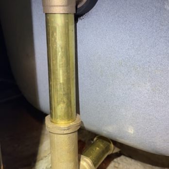 All Rooter - Brand new pipe work - The image shows a close-up of plumbing pipes, including a vertical pipe with a transparent section revealing water inside. The pipes are connected with fittings and are situated near a large metallic or concrete water tank or appliance. The background includes a concrete or stone floor, indicating an indoor or basement setting for plumbing installation. - Plumbing Near Me - Chicago, Illinois
