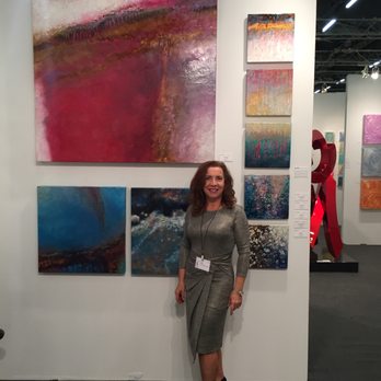 Malton Gallery - Owner Sylvia Rombis with images from one of the 100 artists the gallery represents - Art Galleries Near Me - Cincinnati, Ohio