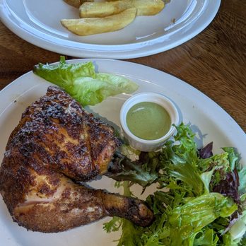 Mister Pio - A meal featuring a grilled chicken leg with a side of mixed greens, a small cup of green sauce, and a plate of potato wedges. - Peruvian Near Me - Phoenix, Arizona