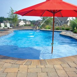Blue Haven Pools - Free-form concrete pool with brick coping, laminar deck jets, and tanning ledge with integrated sun umbrella