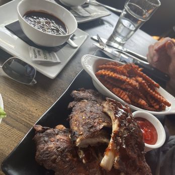 Modern Plate - Ribs, sweet potato fries w/sauce - A meal featuring a large grilled meat chop with sauce, sweet potato fries, and two cups of coffee, served on a black tray and white plates. - Cocktail Bars Near Me - Elmhurst, Illinois