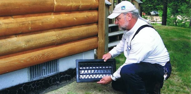 Technician fitting a rodent-proof vent cover at a home's foundation