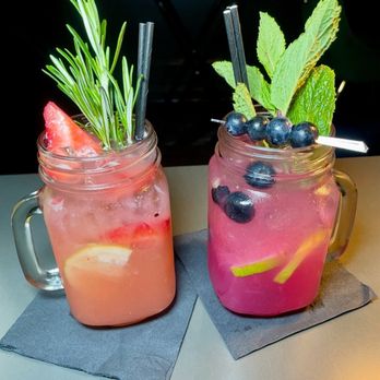 Flavorture - Mocktails - Two vibrant mocktails in mason jars, garnished with herbs and fruit, placed on dark napkins on a table, with a dark background. - Bars Near Me - Washington, DC, District of Columbia