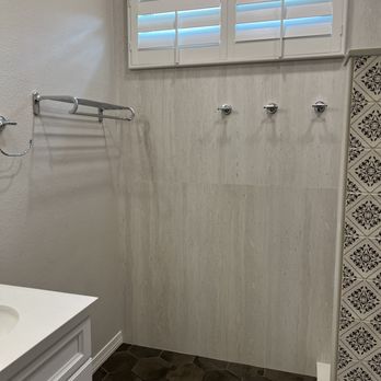 Ruiz Renovation - After - A bathroom corner features a small window with shutters, three towel hooks on the wall, and part of a white vanity with a sink. - Tiling Near Me