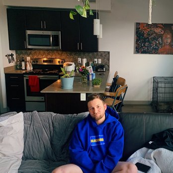 ICO Monteval Apartments Orem - Thomas on the couch with kitchen in the background (he's wearing pants don't worry) - Apartments Near Me - Orem, Utah