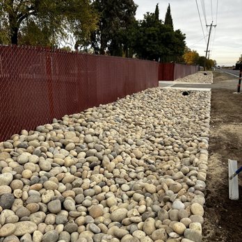 Yard Bros - a pile of rocks next to a fence - Landscaping Near Me