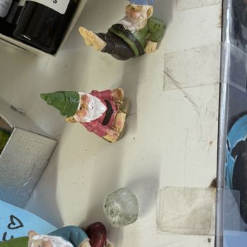 Crystal Dragon - Yoga gnomes (thumb size) - Three garden gnome figurines with colorful hats and beards are arranged on a white surface, with bottles and a glass paperweight nearby. - Jewelry Near Me - Boulder, Colorado