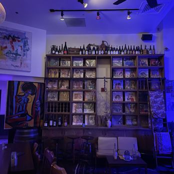 Couchdate - A lounge area with a wooden shelf filled with vinyl records and bottles, illuminated by blue lighting, with artwork on the wall and seating arrangements. - Vinyl Records Near Me - Oakland, California
