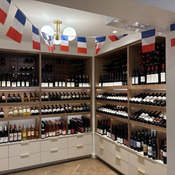 Nouvelle Maison - Wine bottles are arranged on wooden shelves in a retail space, with French flags hanging from the ceiling, indicating a French-inspired theme. - Grocery Near Me - Winchester, Massachusetts