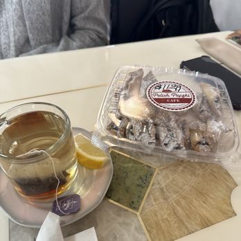 Polish Paczki Cafe - A glass cup of tea with a lemon wedge on a saucer, alongside a box of Polish paczki from Polish Paczki Cafe, on a table with decorative tiles. - Cafes Near Me - Chicago, Illinois