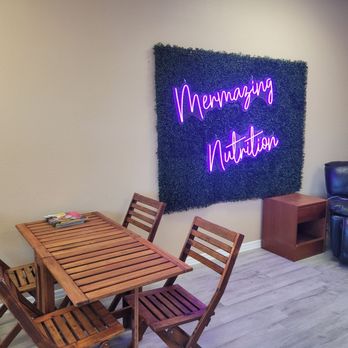 Mermazing Nutrition - The indoor seating for Mermazing Nutrition. A simple table with chairs, a couch, and a lit-up picture display. - Juice Bars & Smoothies Near Me - Melbourne, Florida Mermazing Nutrition - The indoor seating for Mermazing Nutrition. A simple table with chairs, a couch, and a lit-up picture display. - Juice Bars & Smoothies Near Me - Melbourne, Florida