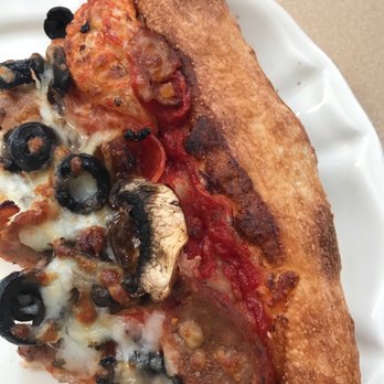 Davidos - A close-up of a pizza slice featuring toppings such as black olives, mushrooms, melted cheese, and tomato sauce. The crust is golden brown and crispy, with some darker spots. The pizza is served on a white, scalloped-edged plate, with a plain background. - Pizza Near Me - Rio Rancho, New Mexico