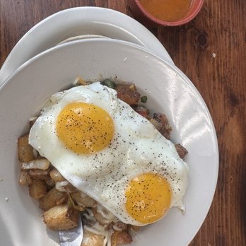 Capsized Cafe - Absolutely wonderful breakfast!  Some. Really cool menu options too! - A breakfast dish featuring two fried eggs on top of potatoes and vegetables, served on a white plate with a side of sauce in a small bowl. - Cafes Near Me - Spring Lake, New Jersey