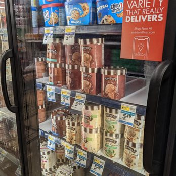 Smart & Final Extra! - Ice cream anyone? - The image shows a refrigerated display case filled with various ice cream and gelato containers from brands such as Dreyer's and Chips Ahoy!. The containers are stacked on shelves, with price tags visible. A red sign on the door promotes delivery options with a website link. The case has a glass door with a handle, and reflections of the store interior can be seen on the glass surface. - Grocery Near Me - Encinitas, California