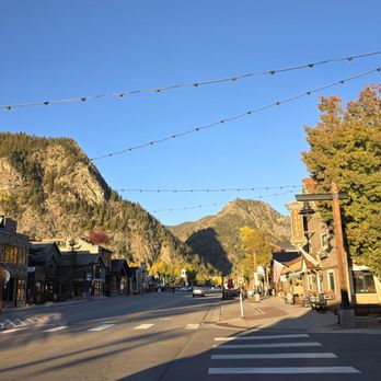 Bread+Salt - Frisco today looking toward west - A street in a mountain town with shops, trees, and string lights, set against a backdrop of mountains and a clear blue sky. - Breakfast & Brunch Near Me - Frisco, Colorado