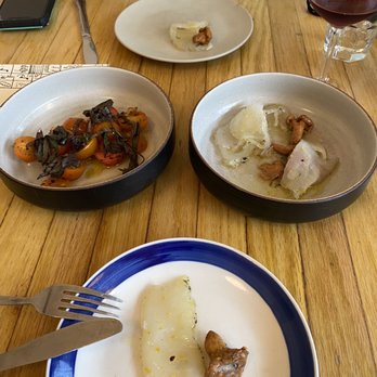 Cellar Door Provisions - Tomatoes and halibut with mushrooms - Three dishes of food, a glass of red wine, and a smartphone are arranged on a wooden table at a restaurant, with a person partially visible. - New American Near Me - Chicago, Illinois
