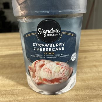 Albertsons - Strawberry Cheesecake Ice cream! - A plastic tub of Signature Select Strawberry Cheesecake ice cream is placed on a wooden table, featuring a label with an image of the ice cream and flavor details. - Grocery Near Me - Mesa, Arizona