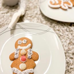 Gingerbread cookie kits!! - A gingerbread cookie shaped like a person, decorated with white icing, candies, and sprinkles, placed on a white plate.