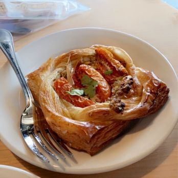 Corvus Coffee Roasters - Savory Pastry (goat cheese and tomatoes) - A pastry filled with goat cheese and topped with tomatoes and herbs, served on a white plate at a restaurant. - Coffee & Tea Near Me - Arvada, Colorado