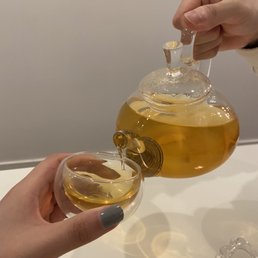 a person pouring tea into a glass cup a person pouring tea into a glass cup