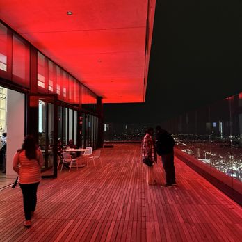 View Boston - Nighttime scene on an outdoor observation deck with glass walls, featuring a few people and city lights visible in the background. - Observatories Near Me - Boston, Massachusetts