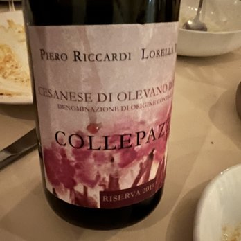 Otway - Delicious wine - A wine bottle with a label indicating 'Piero Riccardi Lorelli' and 'Collepazzo Riserva 2015' is positioned on a dining table. The label features a pinkish design with floral elements. Nearby, there are plates with food remnants, a bowl with a spoon, and cutlery, suggesting a meal setting. - New American Near Me - Brooklyn, New York