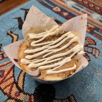 Sugar N Glitz - Pumpkin sour cream muffin - A muffin with white icing drizzle and caramel sauce is placed on a colorful woven fabric with geometric patterns. - Bakeries Near Me