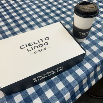 Cielito Lindo Cafe - Dirty chai latte - A white takeout coffee box and a coffee cup with a sleeve are placed on a blue and white checkered tablecloth at Cielito Lindo Café. - Coffee & Tea Near Me - Whiting, Indiana