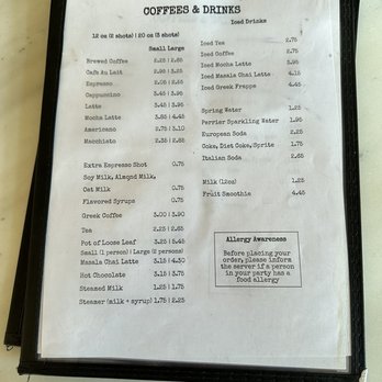 Athan's Bakery - A menu titled 'COFFEES & DRINKS' displays various hot and iced beverages such as brewed coffee, espresso, cappuccino, latte, and iced drinks like iced tea and iced coffee. Prices are listed for each item, with options for different sizes and additional syrups. The menu also includes water, soda, and fruit smoothies, along with allergy awareness instructions. The menu is printed on white paper and placed inside a black folder on a table. - Bakeries Near Me - Brookline, Massachusetts