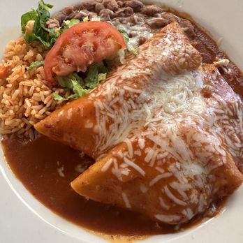 La Cueva Cafe - Chicken enchiladas with red - A white plate holds a serving of cheese enchiladas topped with melted cheese and sauce, accompanied by rice, refried beans, and a small side salad with lettuce, tomato, and salsa. The dish is typical of Mexican cuisine and is presented with a variety of textures and flavors. - Mexican Near Me - Taos, New Mexico