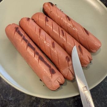 Zwilling - Hot doggity dawg!! - Four grilled hot dogs with grill marks are arranged on a light green plate, with a knife placed on the right side. - Kitchen Supplies Near Me - Rosemont, Illinois