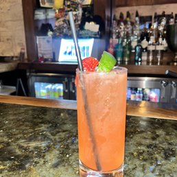 Strawberry Limeade - A pink-colored cocktail with ice, garnished with a strawberry and lime wedge, placed on a bar counter with a straw.