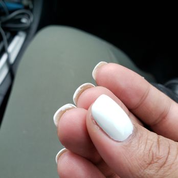 High Tech Nails - The image shows a close-up of a hand with well-maintained nails painted white. Some nails have chipped polish, revealing the natural nail underneath. The background is blurred, with a hint of a car interior, including a seat and some electronic cords. The focus is on the nails and fingers, highlighting the manicure and the chipped polish. - Nail Salons Near Me - Normal, Illinois