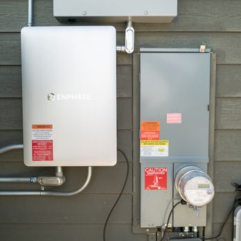 Connected Technology - Enphase combiner - A white Enphase combiner box and an electrical meter are installed on an exterior wall, with warning labels and electrical conduit connections. - Electricians Near Me - Rocklin, California