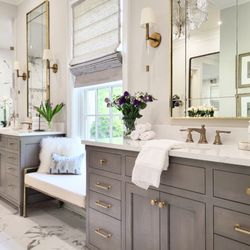 One Coast Design - Taupe based stain on quartersawn oak cabinetry, marble counter tops, marble flooring tile, sconce lighting flanking mirrors and a window...